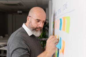 Homem em frente a um quadro Scrum com colunas de tarefas, representando ciclos de sprints no desenvolvimento ágil